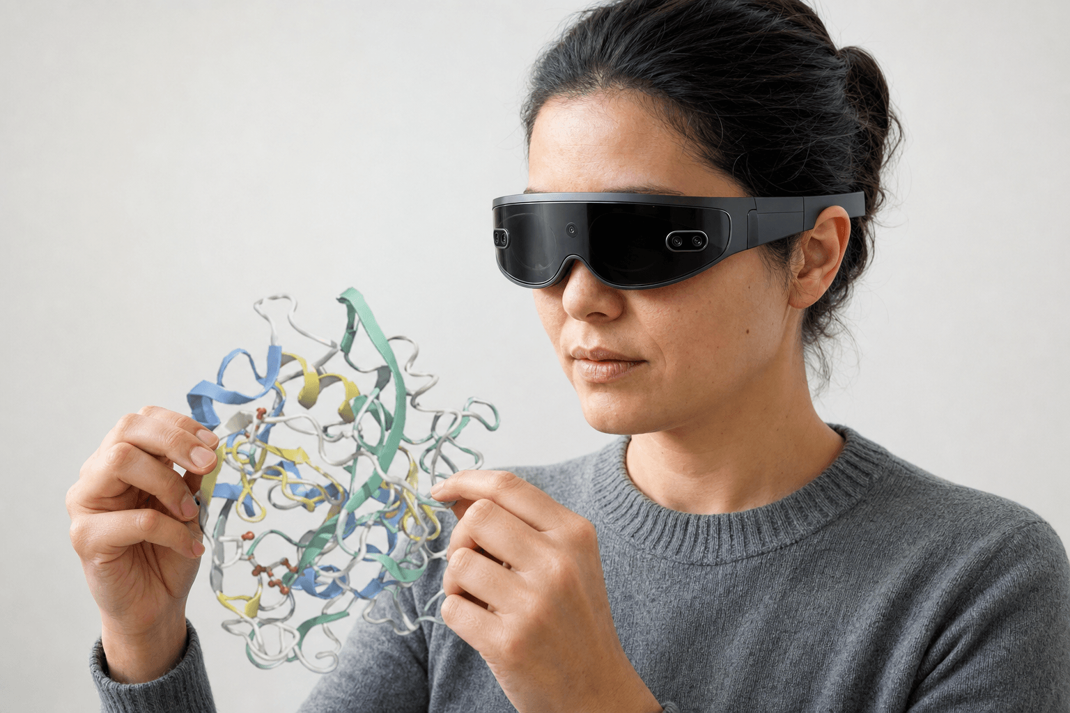 A researcher wearing an ultra-thin VR headset studies a ribbon-cartoon protein structure held close to the chest