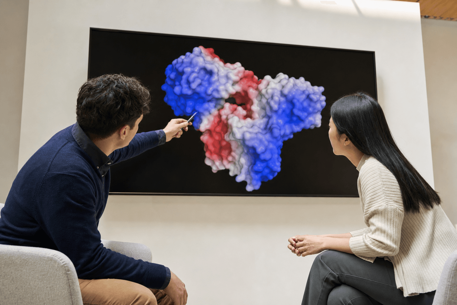Two researchers review an antibody binding interface rendered as a molecular surface on a large wall display, one pointing to the binding pocket.